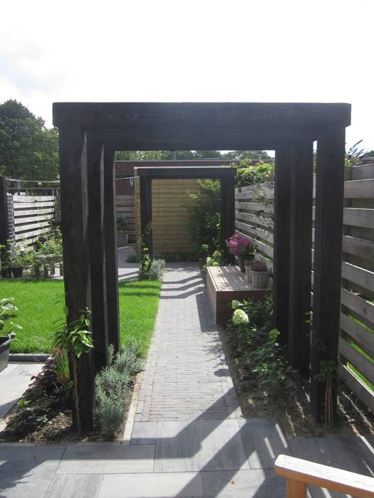 De moderne antraciet Douglas houten pergola die voor de verbinding en diepte in de tuin. Rechts tegen de schutting een hardhouten bank die tevens ook als opslag dient voor speelgoed. Van Dijk Tuinen Groningen Moderne tuinen pergola,modern,strak