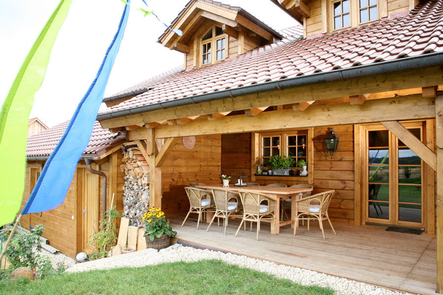 BayernBlock-Blockhaus aus Kantholzbalken "Kösslinger" – Veranda BayernBlock Holzbau GmbH & Co. KG - HultaHaus Balkon, Veranda & Terrasse im Landhausstil Anlage,Gebäude,Eigentum,Fenster,Tisch,Sessel,Holz,Schatten,Blumentopf,Hütte