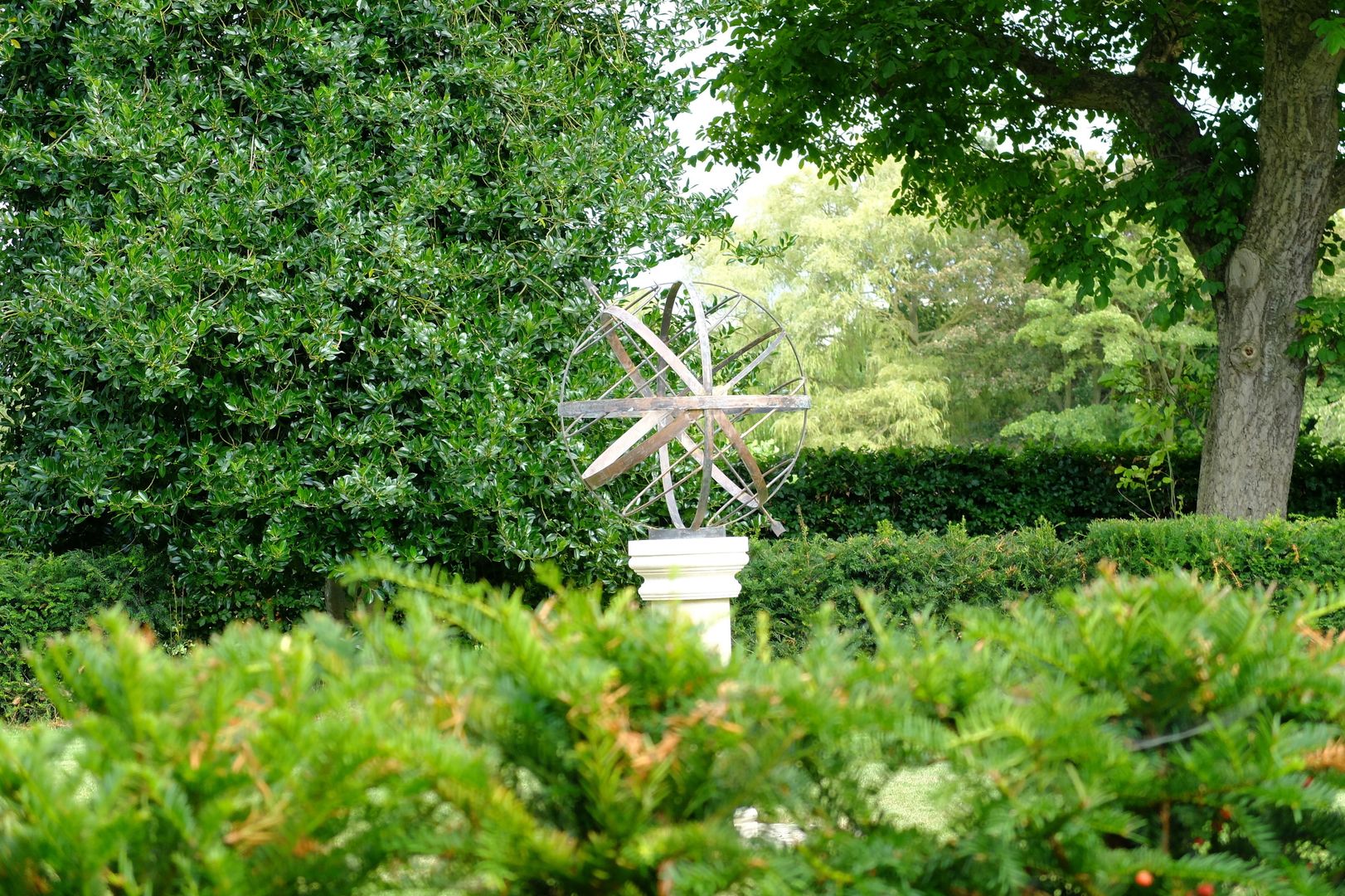 Verdigris armillary behind an evergreen hedge Border Sundials Ltd Jardines clásicos Decoración y accesorios