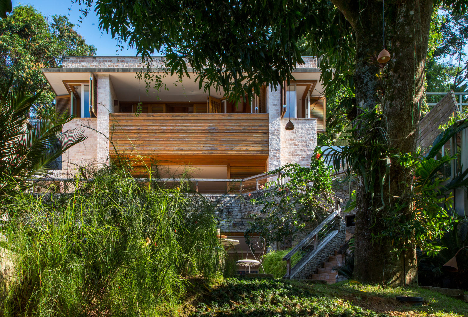 FACHADA Maria Claudia Faro Casas tropicais fachada tijolo,tijolo aparente,escada externa,casa em desnivel,painel de madeira,janela esquina,janela camarão,jardim,varanda,beiral,marquise