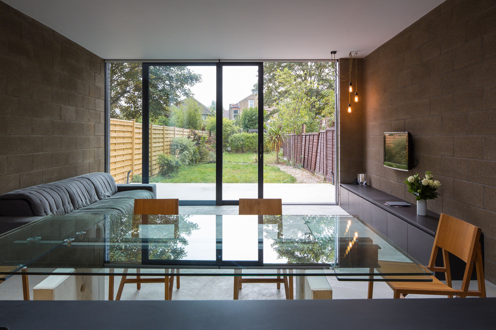 View over dining table with living area and garden beyond Mustard Architects Salas de jantar industriais