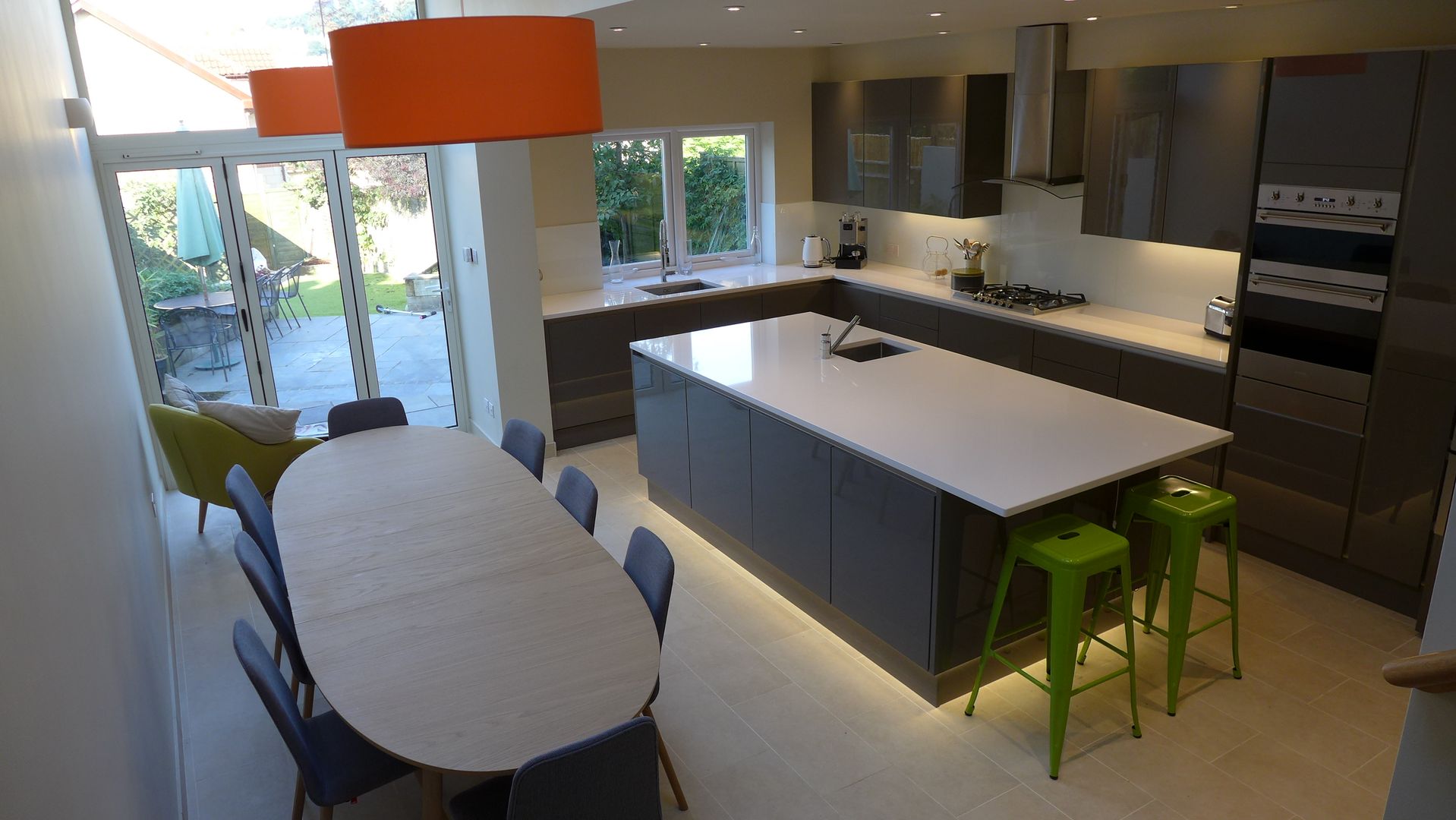 Gloss grey kitchen in open plan kitchen diner Style Within Cocinas de estilo moderno gloss,grey,kitchen,open plan,quartz,white worktop,glass kitchen splashback,eye level oven,gas hob,cooker hood,plinth lighting,porcelain floor tiles