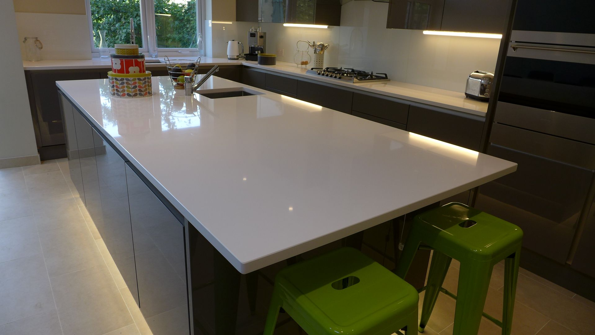 Gloss grey kitchen island with white quartz worktop Style Within Moderne keukens gloss,grey,kitchen,open plan,quartz,white worktop,glass kitchen splashback,eye level oven,gas hob,cooker hood,plinth lighting,porcelain floor tiles