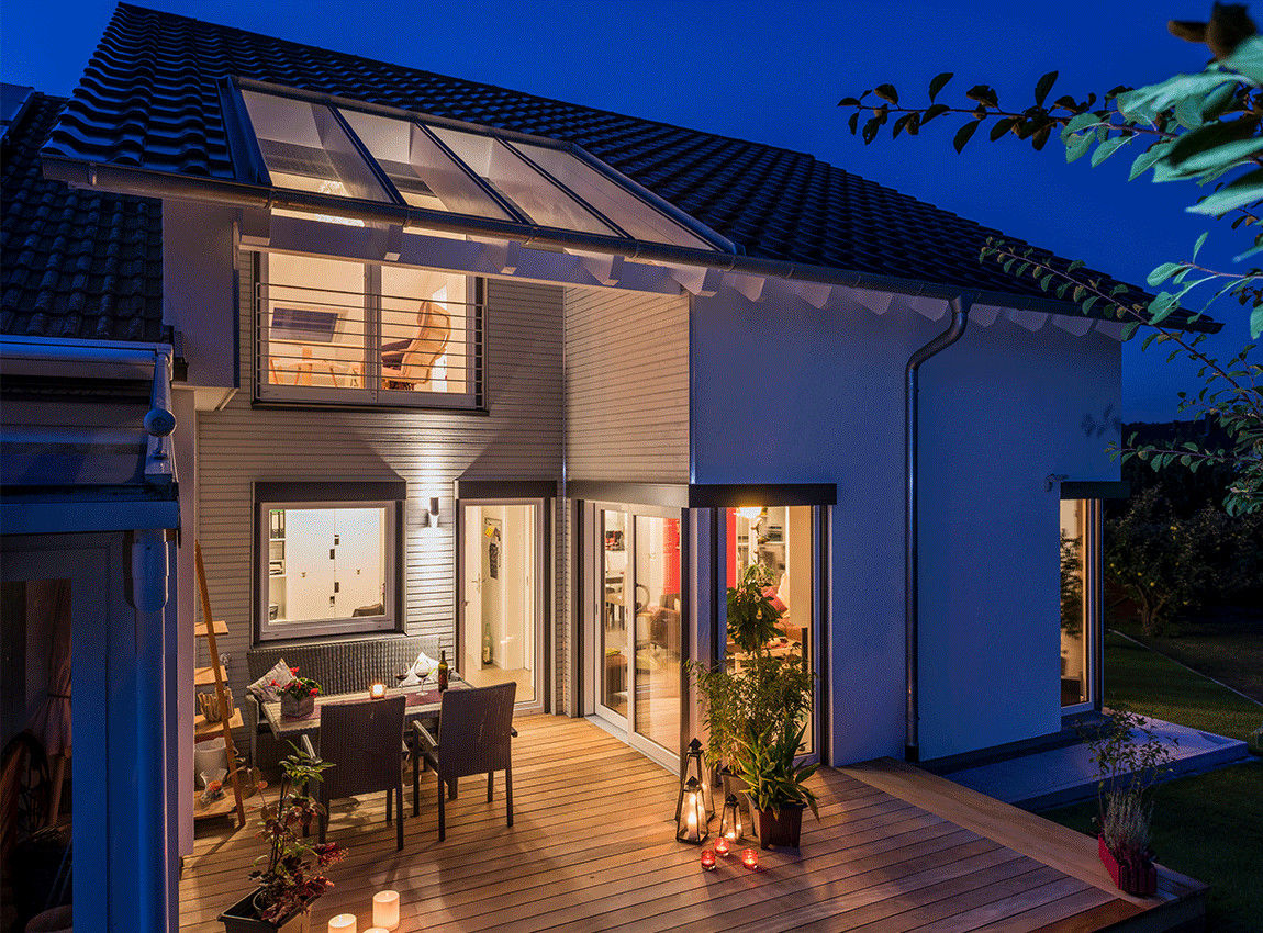 Gemütliche Terrasse mit Glasdach in den Abendstunden KitzlingerHaus GmbH & Co. KG Fertighaus Holzwerkstoff Transparent KitzlingerHaus,Fertighaus,Holzhaus,Ökokaus,Anbau,Terrasse,Glasdach,Holzfassade