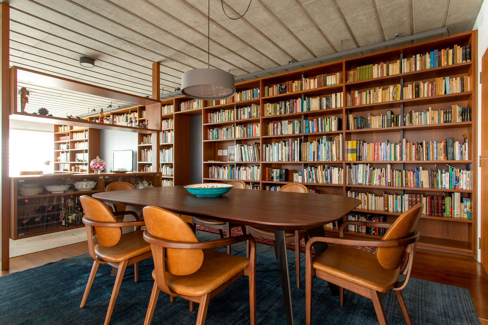 Sala de jantar com biblioteca de livros Estudio Piloti Arquitetura Salas de estar modernas Madeira Acabamento em madeira