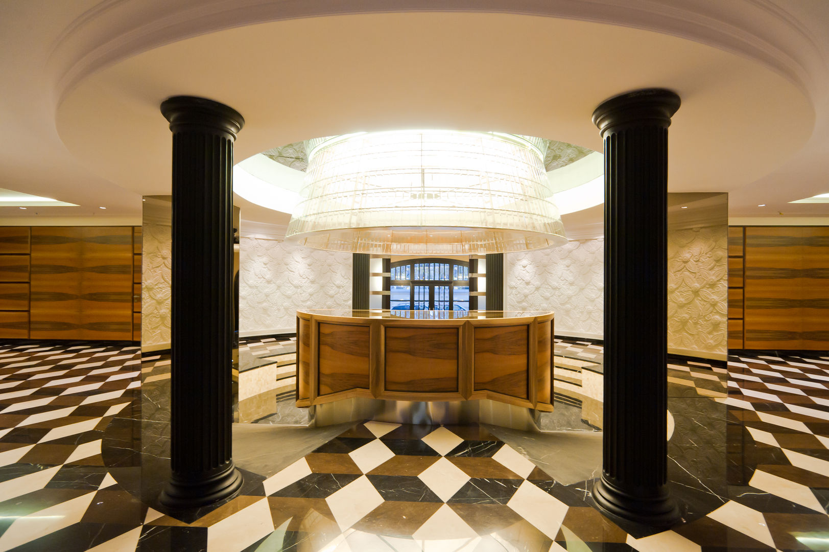 Curved reception desk in walnut color, doric columns in black lacquered wood, Boiserie and sunblinds in colored walnut, white lacquered Boiserie with floral-themed inlays, custom chandelier in steel and beveled crystals above a reception desk Tognini Bespoke Furniture Oficinas Madera Acabado en madera Escritorios